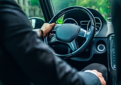 Close up view of young man in formalwear keeping hand on the steering wheel while driving