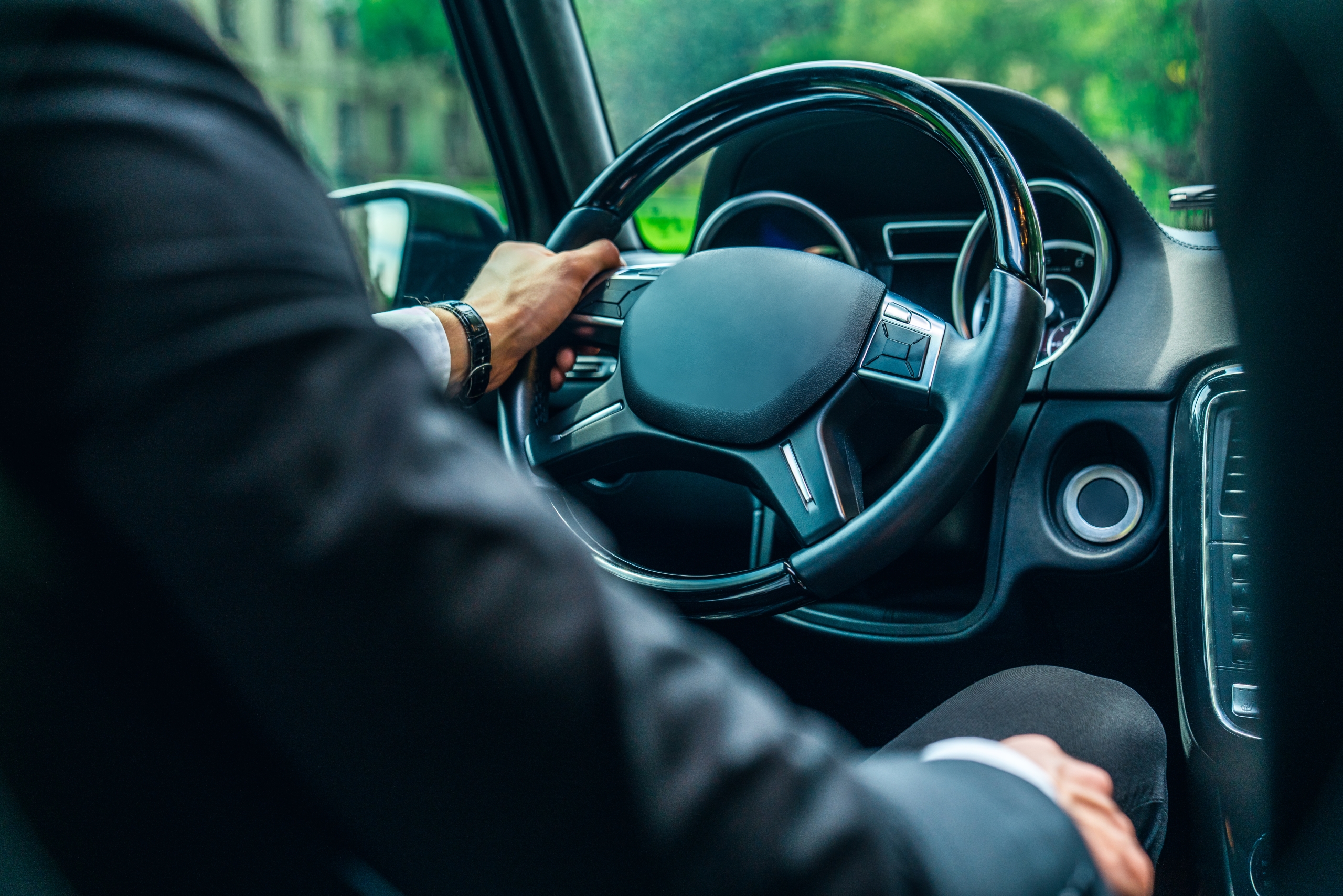 Close up view of young man in formalwear keeping hand on the steering wheel while driving